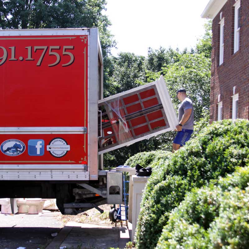 mover loads a cabinet into the back of a red moving truck