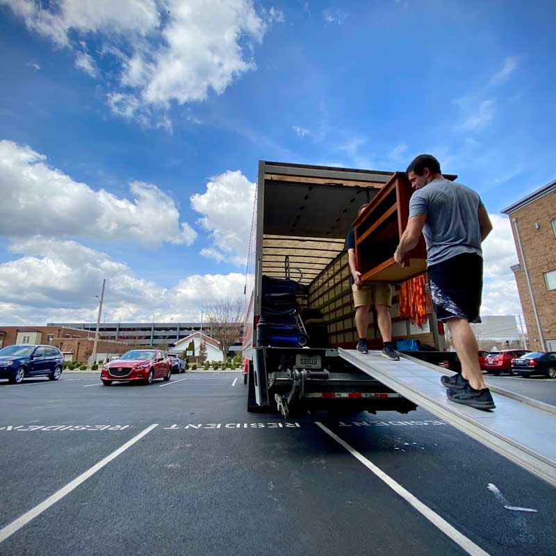 two movers loading a wooden table into a moving truck